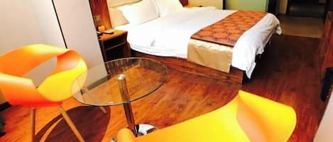 Une chambre d’hôtel avec un lit, une table en verre et deux chaises orange.