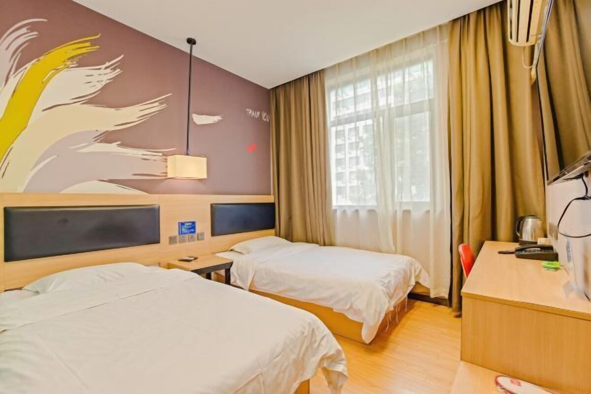Une chambre d’hôtel avec deux lits, un bureau, une lampe, une grande fenêtre avec des rideaux et une fresque murale.