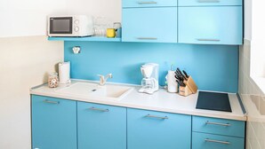 Una cocina compacta con armarios azules, una encimera blanca, un microondas, una cafetera y un bloque de cuchillos.