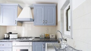 A kitchen with light blue cabinets, a gas stove, an oven, a sink with a metal rack, and a window above the sink. - Wonderful private villa for 3 guests with WIFI, TV, terrace, pets allowed and panoramic view (Castellaro)