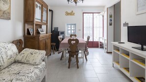 A cozy living room with a sofa, dining table, chairs, a TV, and a bookshelf. - Wonderful private villa for 3 guests with WIFI, TV, terrace, pets allowed and panoramic view (Castellaro)