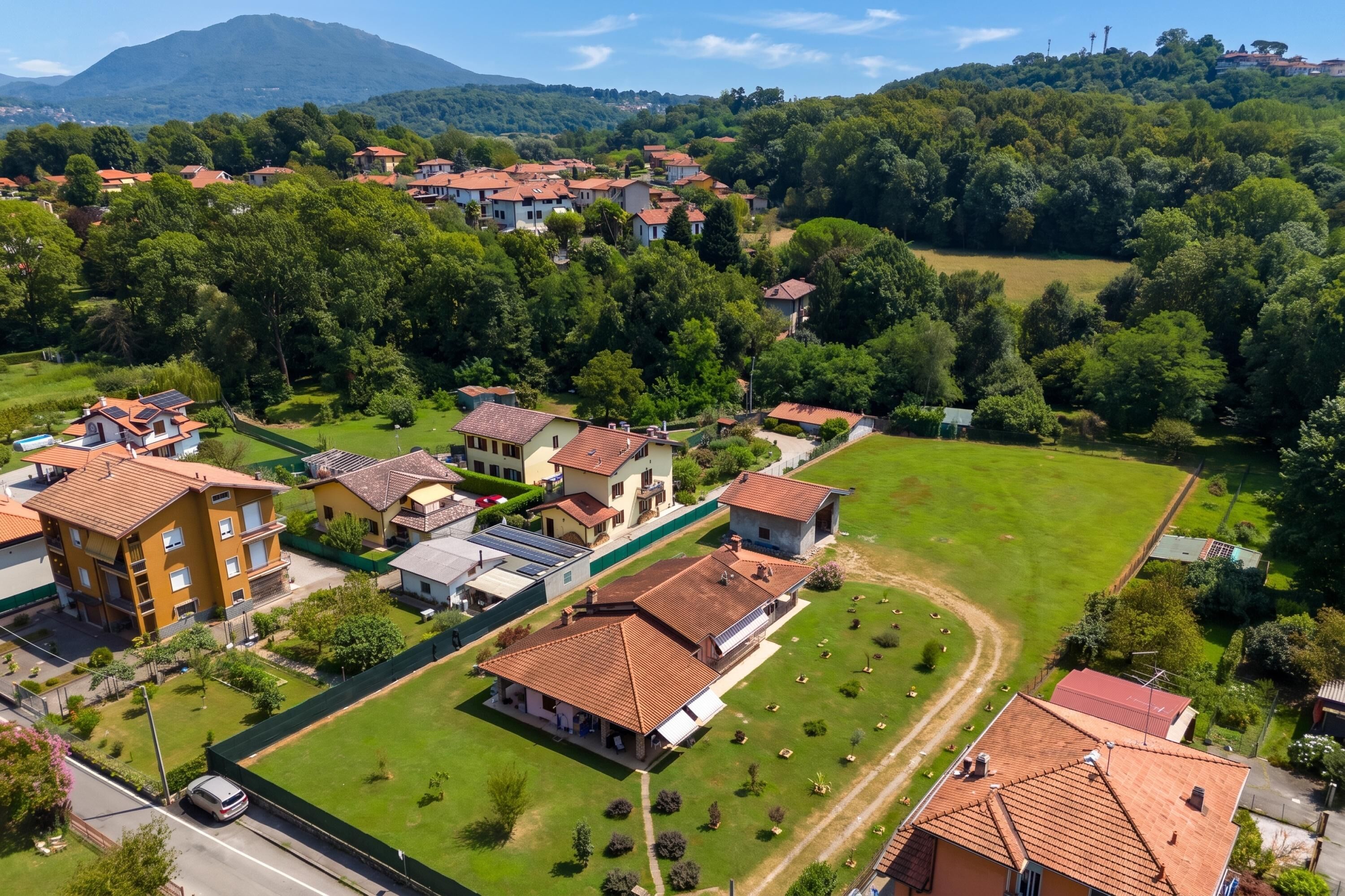 A residential area with houses, a green field, and a mountain in the background.