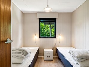 Two single beds with neatly folded linens, a bedside table, and a window with a wall-mounted light fixture.