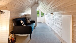 A cozy cabin interior with a wooden ceiling, a sofa with cushions, a small table, and a window overlooking greenery. - "Laerke" - 200m from the sea by Interhome (Gudhjem)