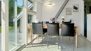 A dining area with a wooden table and four chairs, large windows, and a ceiling light fixture. - "Laerke" - 200m from the sea by Interhome (Gudhjem)