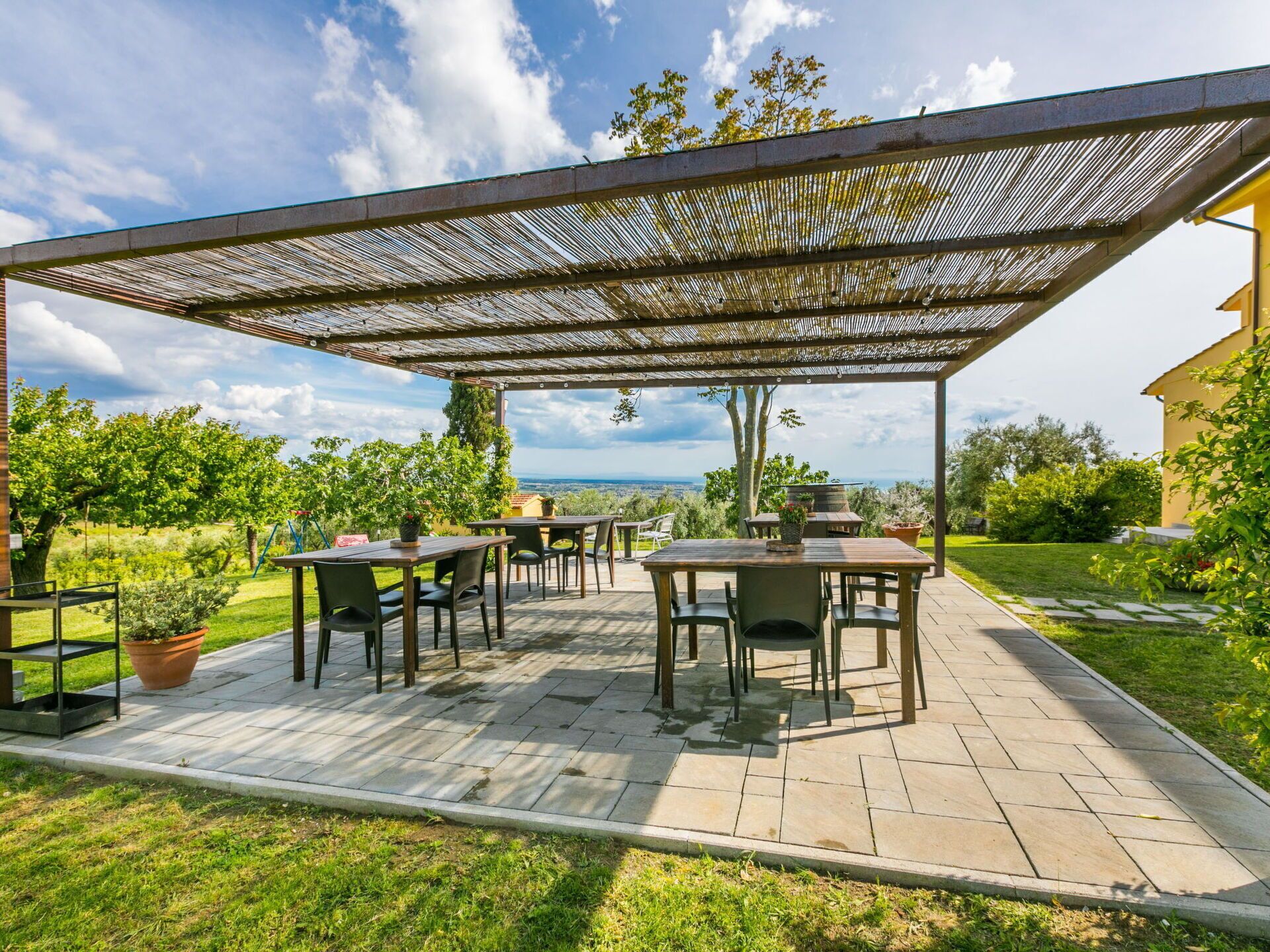 An outdoor patio with tables and chairs, a pergola, and a view of the countryside.