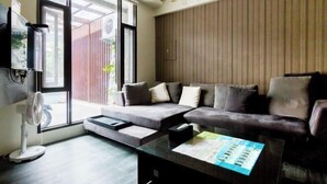 Ein modernes Wohnzimmer mit einem Ecksofa, einem Glastisch und einem großen Fenster, das für natürliches Licht sorgt.