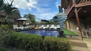 Un área de piscina con sillas de descanso, una estatua y un edificio con balcón.