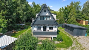 Une maison à deux étages dotée d’un balcon, entourée d’un jardin bien entretenu et d’arbres.