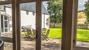 A view through a glass door into a patio area with outdoor seating and a grassy lawn. - Stunning private villa for 10 guests with WIFI, TV, terrace and pets allowed (Corrimony)