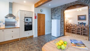 A modern kitchen with white cabinetry, a built-in oven, microwave, and a stainless steel range hood. There's a stone wall and wooden ceiling beams, and a dining area with a table and chairs. - Stunning private villa for 10 guests with WIFI, TV, terrace and pets allowed (Corrimony)