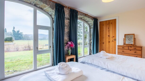 A bedroom with a large window, a wooden dresser, and a bed with white linens. - Stunning private villa for 10 guests with WIFI, TV, terrace and pets allowed (Corrimony)