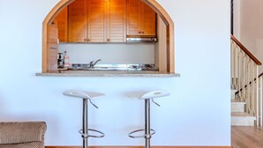 A kitchen with wooden cabinets, a stainless steel sink, and a built-in archway. There are two bar stools in front of the kitchen. - Lovely apartment for 4 guests with WIFI, A/C, TV and terrace (Ispra)