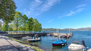 A marina with boats docked, a stone pathway, and a view of the water and hills in the background. - Lovely apartment for 4 guests with WIFI, A/C, TV and terrace (Ispra)