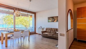 A modern living room with a dining area, large windows, and a view of the outdoors. - Lovely apartment for 4 guests with WIFI, A/C, TV and terrace (Ispra)