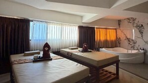 A hotel room with two beds, a massage table, a bathtub, and a large window with curtains. - Kebayoran Park Hotel (South Jakarta)