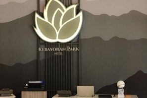 Un comptoir d’accueil surmonté d’un logo, un mur décoré d’un motif de montagne et une enseigne indiquant « Hôtel Kebayoran Park ».