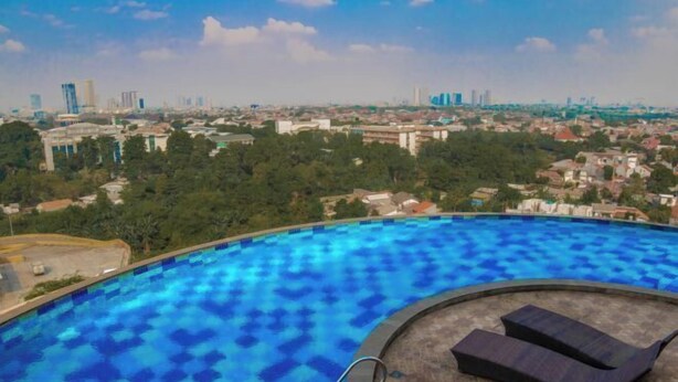 A swimming pool with a city view, lounge chairs, and a clear sky. - Kebayoran Park Hotel (South Jakarta)