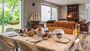 Zona de menjador amb una taula preparada per a quatre, un model de vaixell i un gran finestral amb vistes a la vegetació.