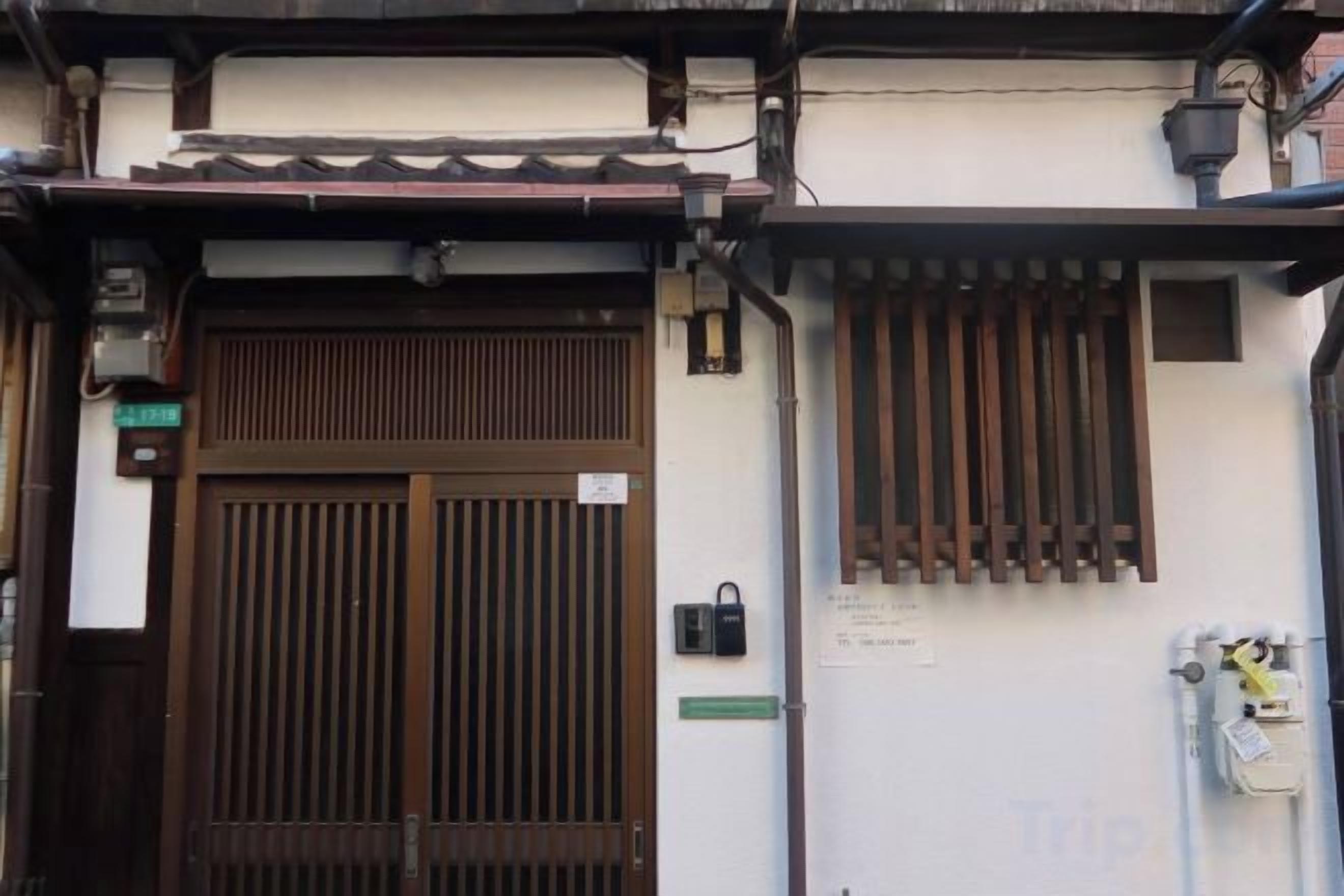 A traditional Japanese gate with a sliding door, a small window with vertical slats, and a wall-mounted light fixture.