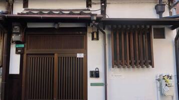 A traditional Japanese gate with a sliding door, a small window with vertical slats, and a wall-mounted light fixture.