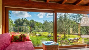 Habitació amb una finestra gran que dona a un jardí amb balançà i gandules.