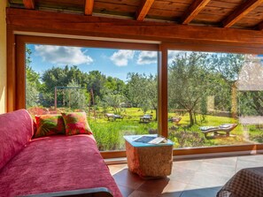 Ein Zimmer mit großem Fenster und Blick auf einen Garten mit Schaukel und Liegestühlen.