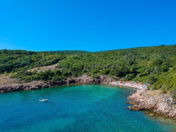Eine Küstenlandschaft mit klarem türkisblauem Wasser, felsigen Ufern und bewaldeten Hügeln im Hintergrund.