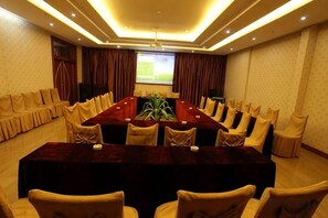 A conference room with a long table, chairs, a projector screen, and a plant. - Shenzhou Hotel (Xiangyun)