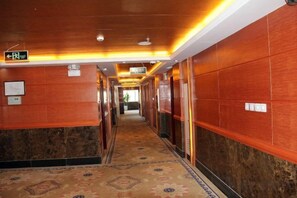 A hotel corridor with a patterned carpet, wooden walls, and a ceiling with recessed lighting. - Shenzhou Hotel (Xiangyun)