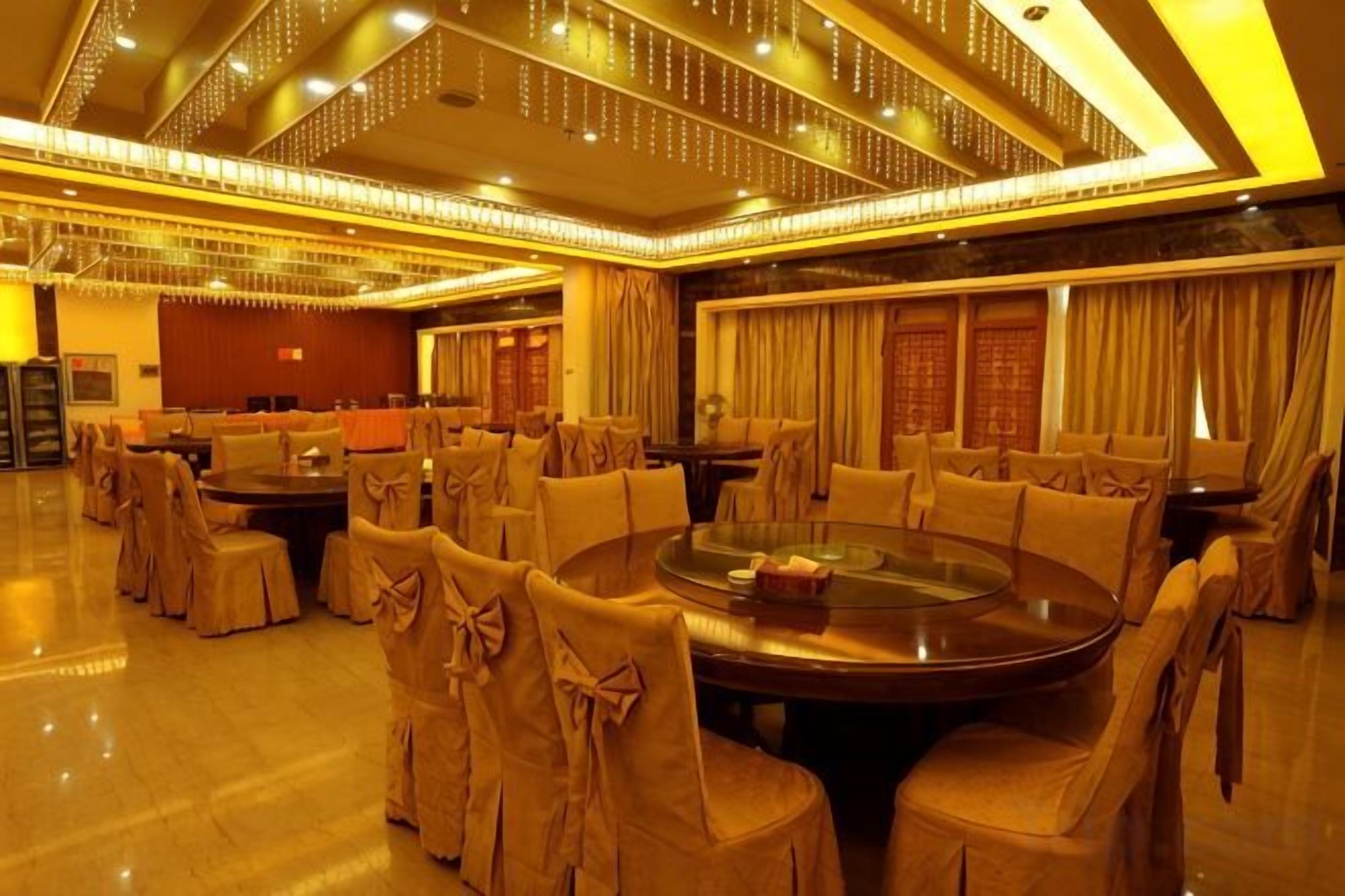 A spacious banquet hall with round tables and chairs, a high ceiling with decorative lighting, and a polished floor.