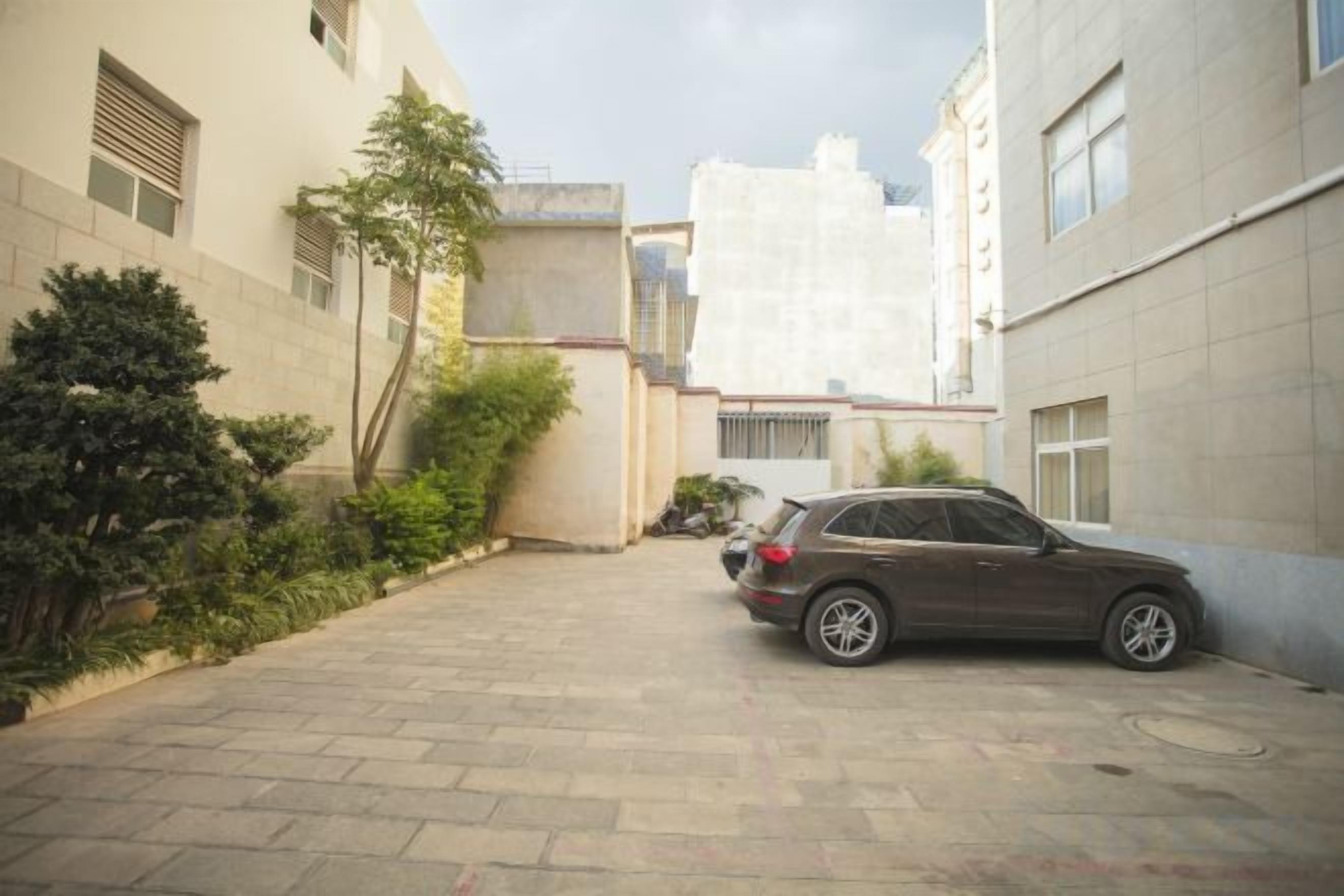 A paved courtyard with a parked car, surrounded by buildings with windows and doors.