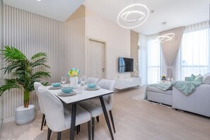 A modern living room with a dining area, a flat-screen TV, and a large window with curtains. - Modern 1BR Dania 1 Apartment with Private Balcony (Dubai)