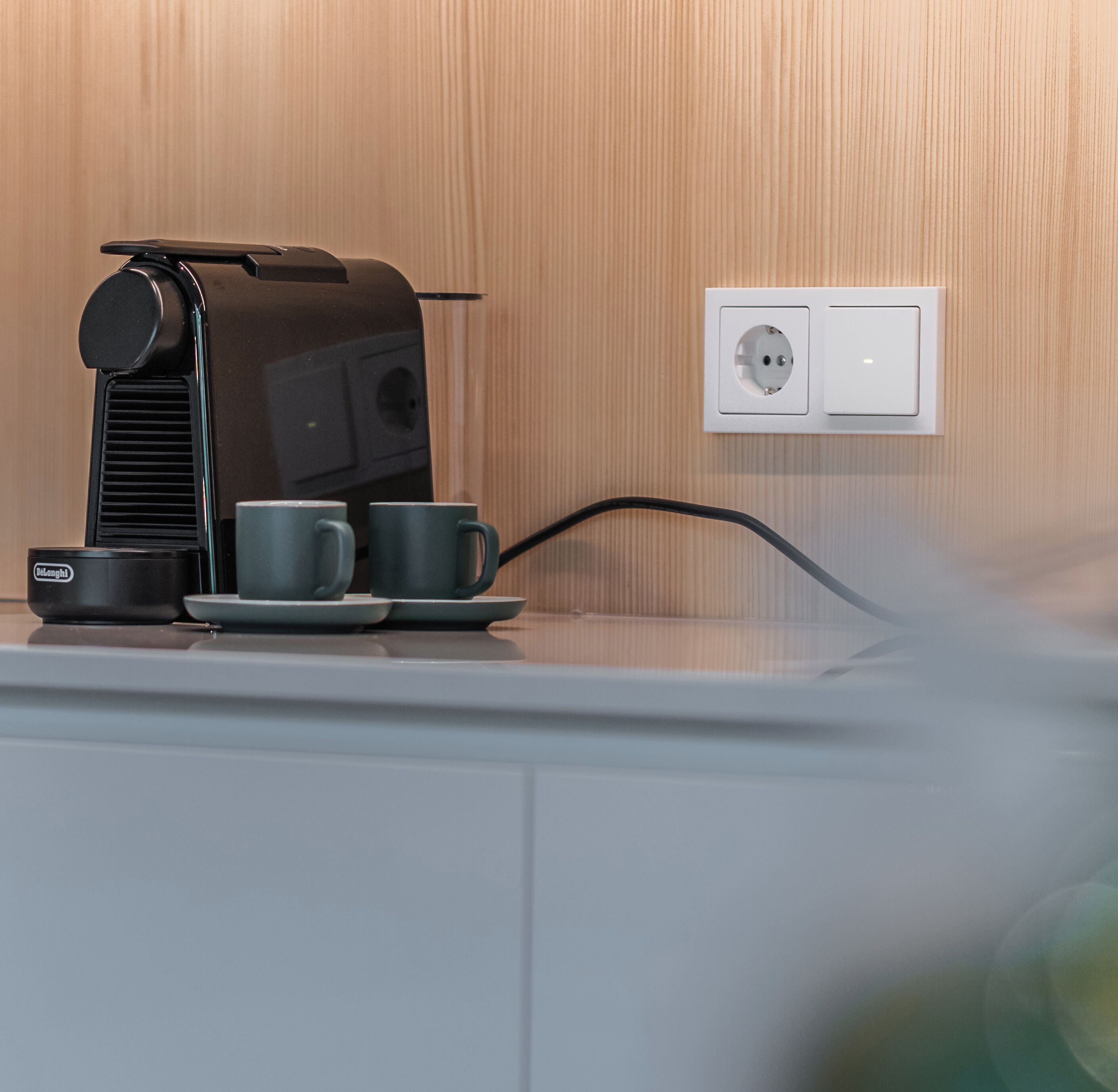 Een koffieapparaat met twee kopjes en een bord op een aanrecht, aangesloten op een stopcontact.
