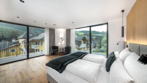 Ein modernes Schlafzimmer mit einem großen Bett, Blick auf eine Wohngegend und einer kleinen Sitzecke mit Tisch und Stühlen.