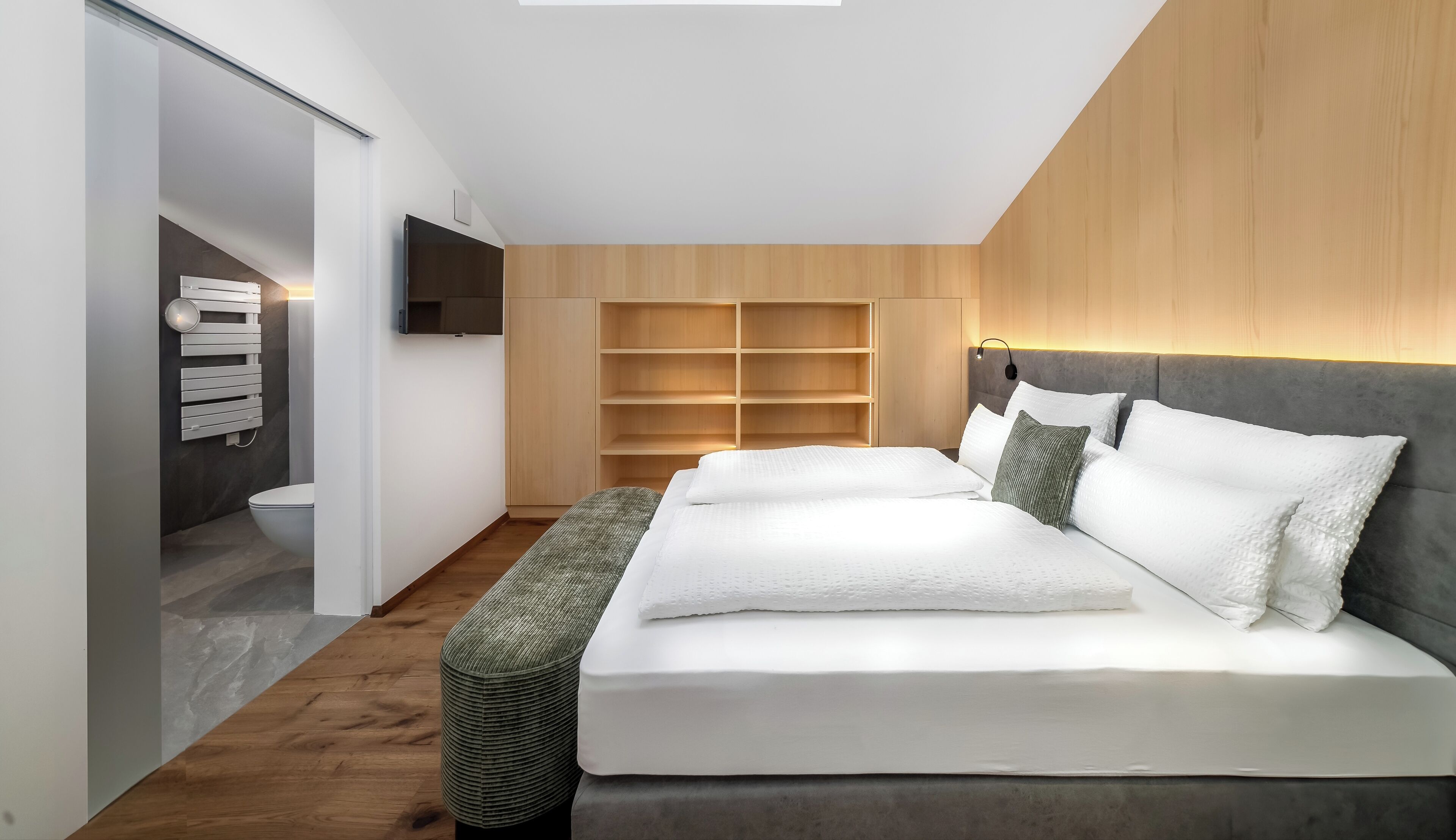 Ein modernes Schlafzimmer mit einem großen Bett, integrierten Regalen, einem Flachbildfernseher und einem Holzkopfteil.