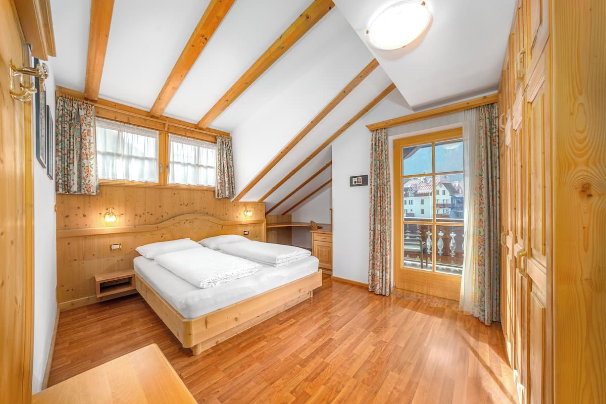 Un dormitorio con techo de madera, una cama, una ventana con cortinas y vistas a edificios.