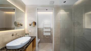 Un baño moderno con lavamanos de mármol, un espejo grande y una cabina de ducha de vidrio.