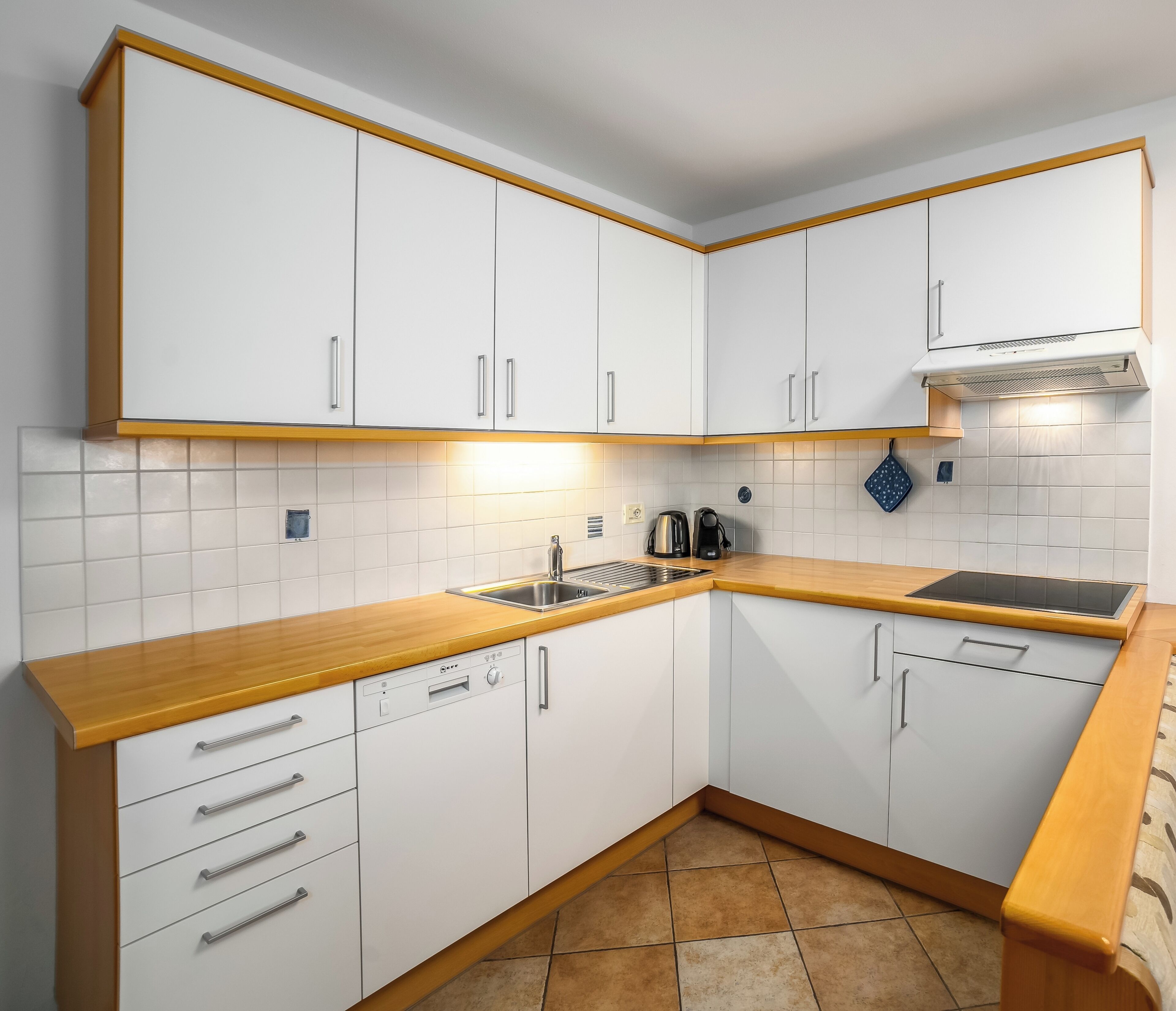 A modern kitchen with white cabinets, a wooden countertop, and a built-in dishwasher.