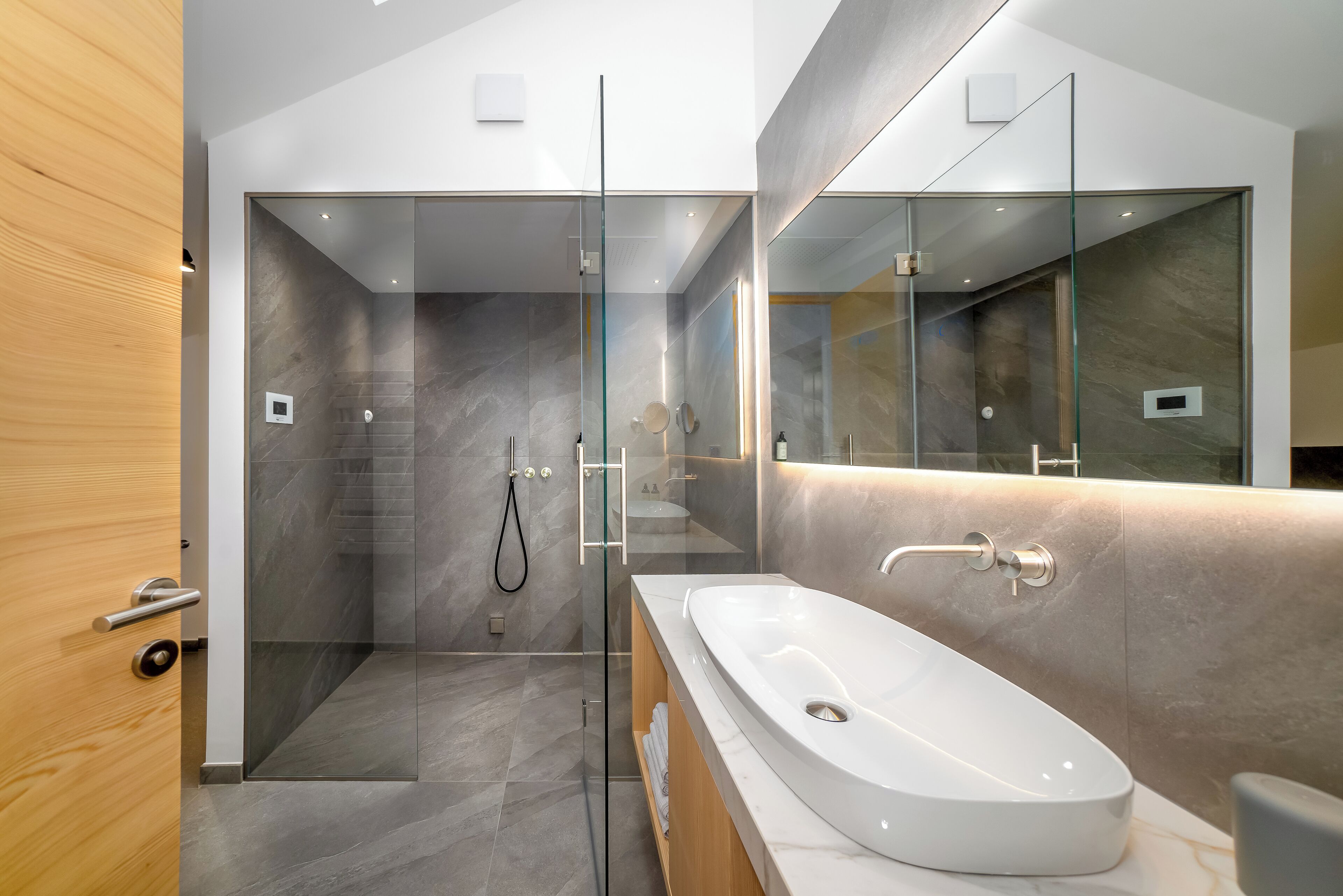 A modern bathroom with a glass-enclosed shower, a large white sink, and a wooden vanity.