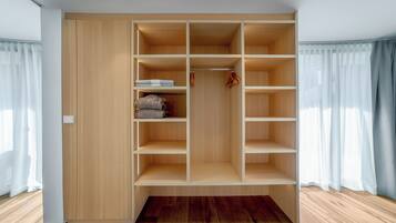A walk-in closet with multiple shelves and hanging space, wooden flooring, and a window with curtains.