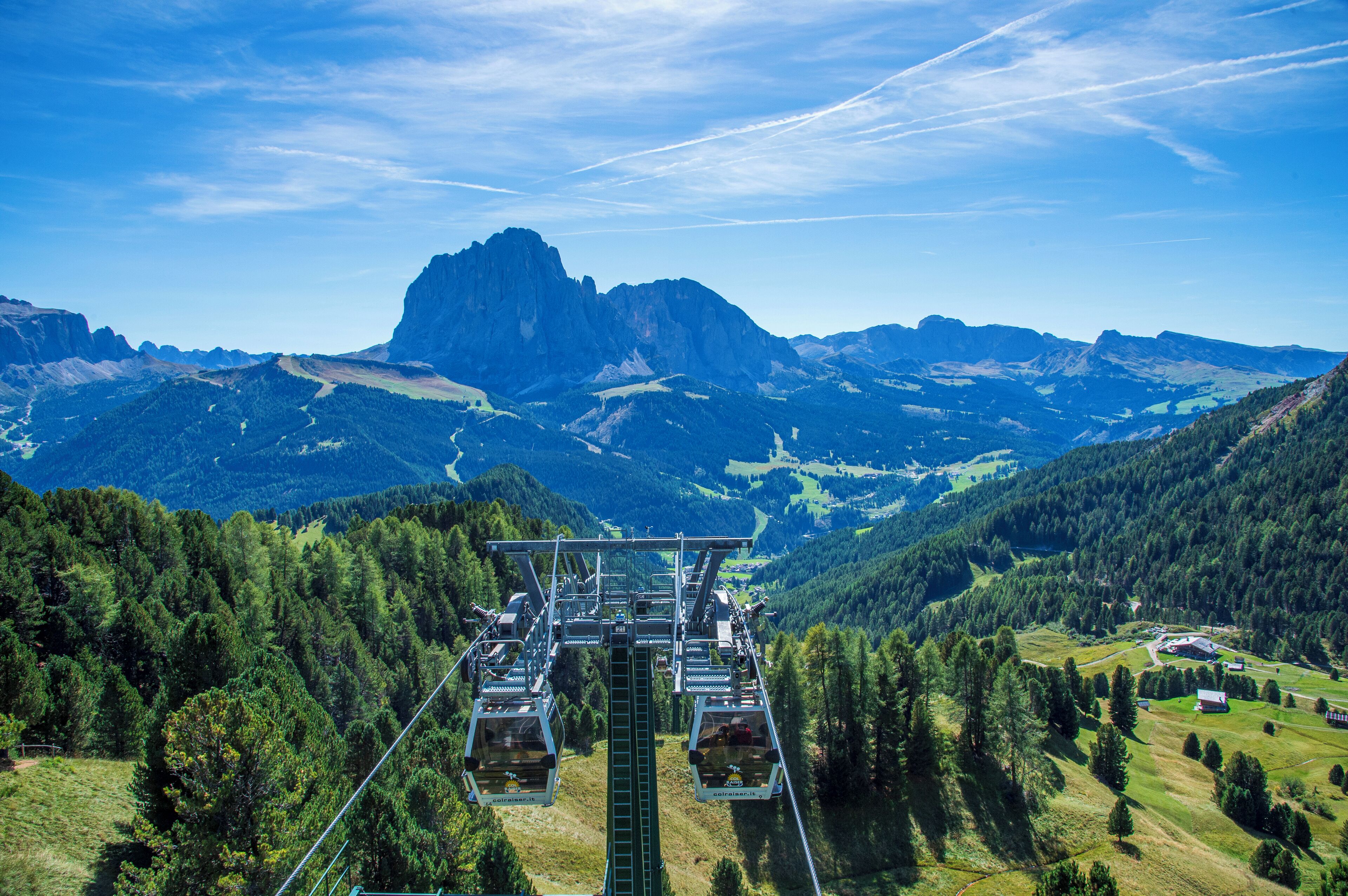 Eine Seilbahnanlage mit Gondeln, einem Berg im Hintergrund und blauem Himmel.