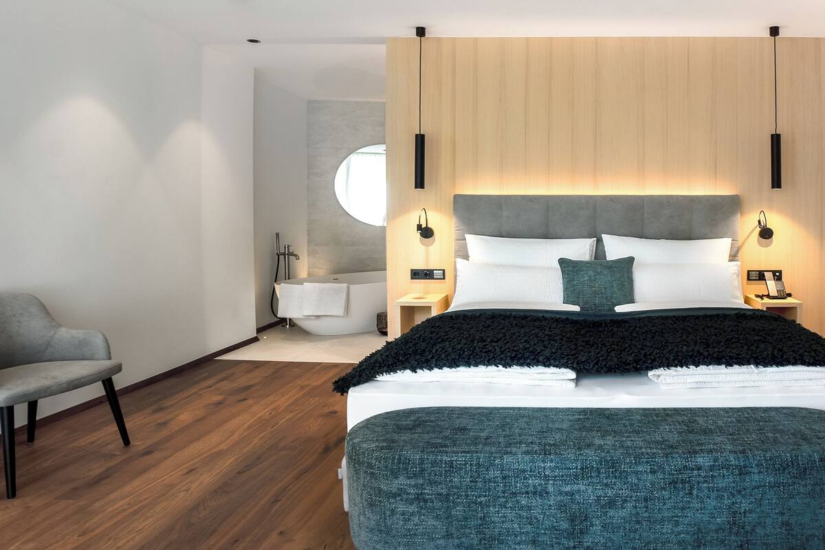 Un dormitorio moderno con una cama grande, una silla y un baño al fondo.