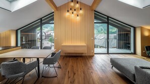 Ein modernes Interieur mit Holzboden, Oberlichtern, einer zentralen Sitzecke und großen Fenstern mit Blick ins Freie.