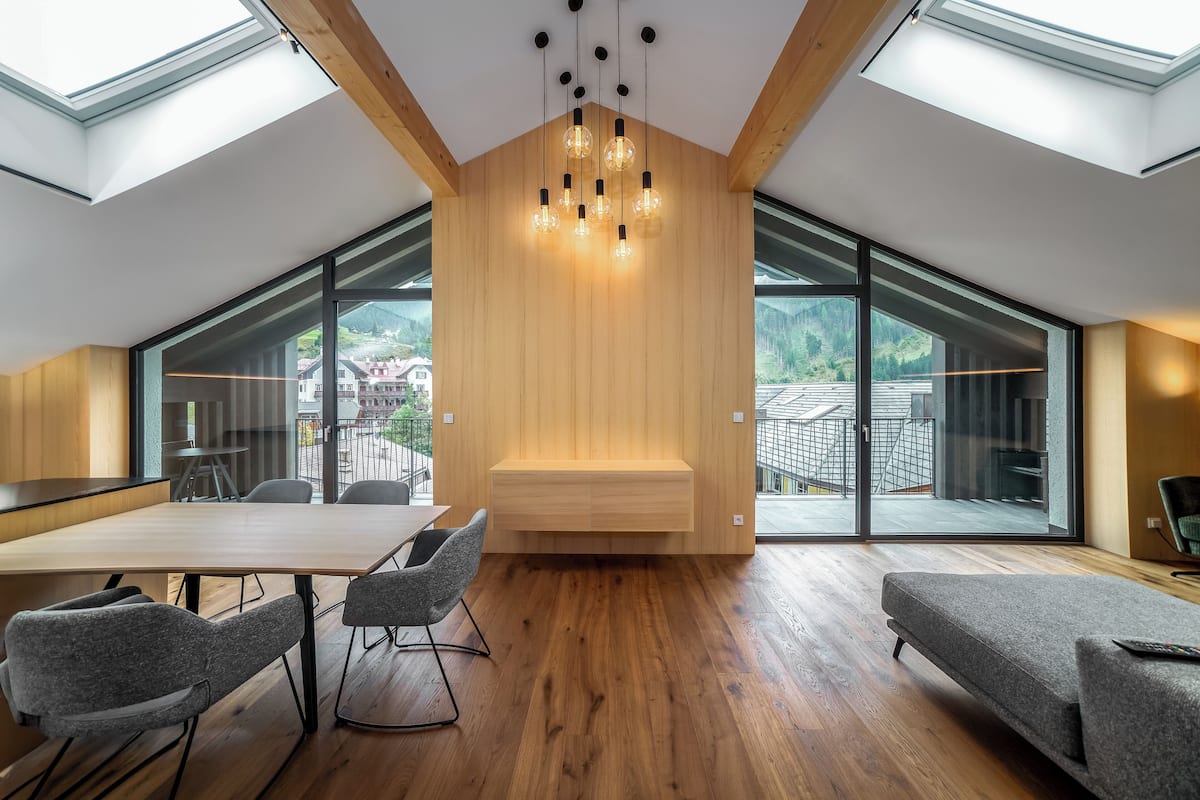 Un interior moderno con techo de madera, tragaluces, un área de estar central y amplios ventanales con vistas al exterior.