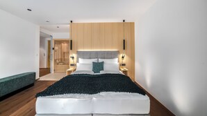 Ein modernes Schlafzimmer mit einem großen Bett, einem Holz-Kopfteil, Nachttischlampen und einer grünen Bank.