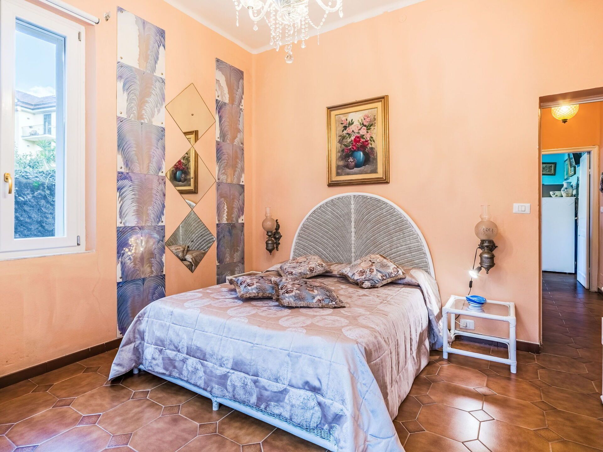 Un dormitorio con cama, una araña, una pared con espejos decorativos y un cuadro.
