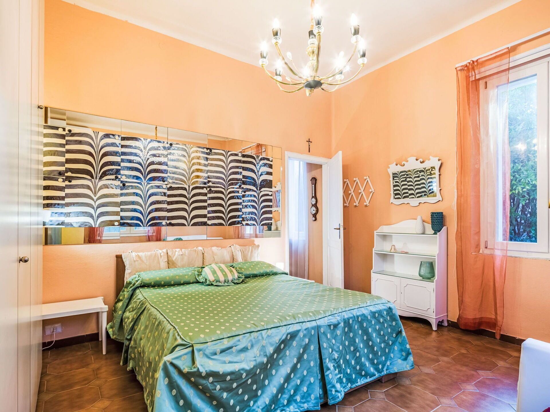 A bedroom with a bed, a chandelier, a wardrobe, and a window with curtains.