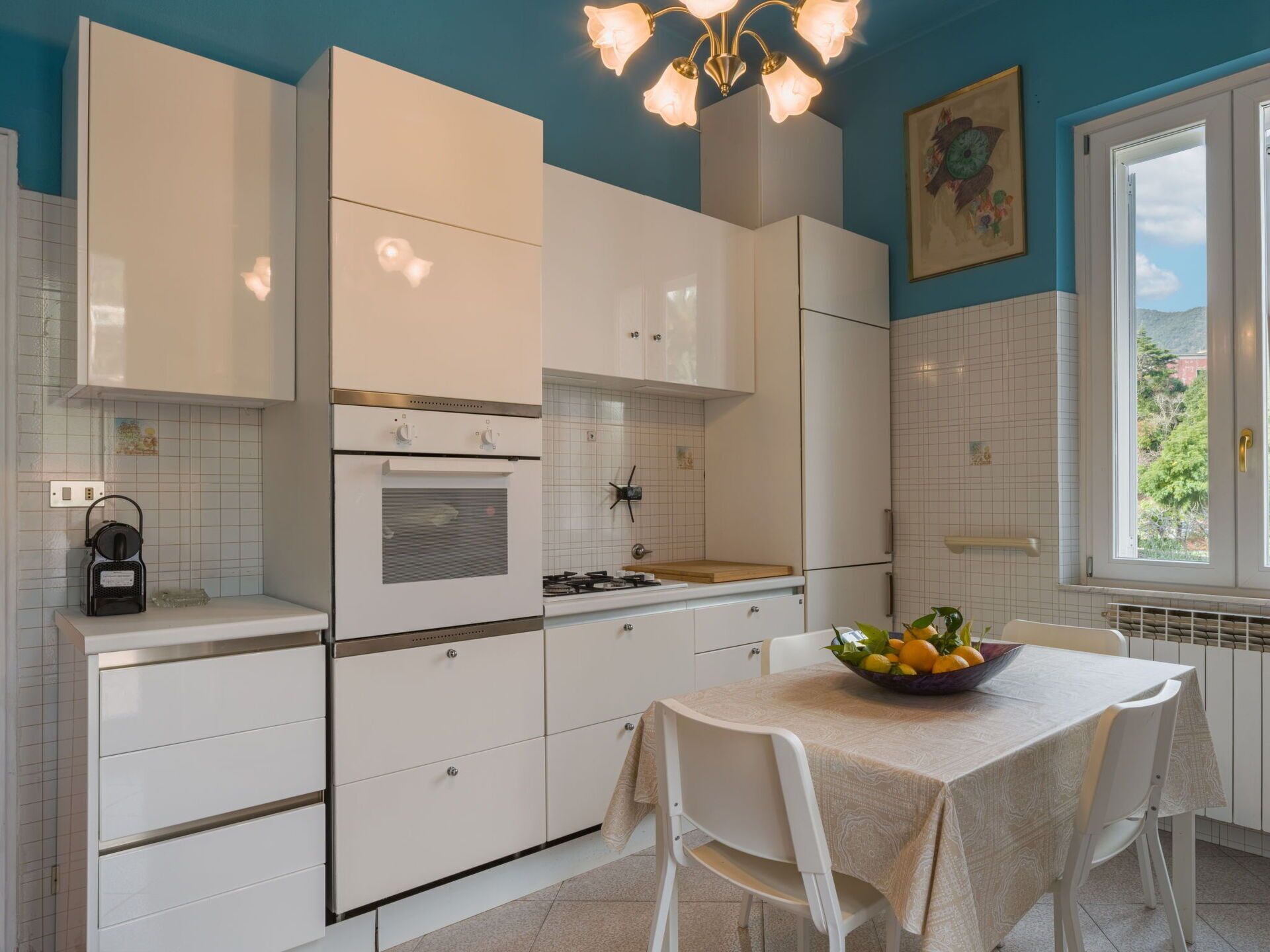 Une cuisine moderne avec des meubles blancs, une cuisinière à gaz et une table à manger agrémentée d’un panier de fruits.