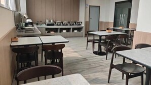 A modern dining area with multiple tables and chairs, a kitchen area with appliances, and a door leading to another room. - HanTing Hotel (Zhengzhou Railway Station Dehua Street) (Zhengzhou)